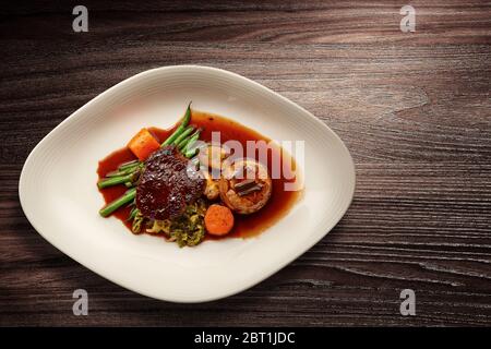 Directement au-dessus d'une élégante assiette de nouvelle cuisine de bœuf et de légumes et de sauce sur fond de bois Banque D'Images