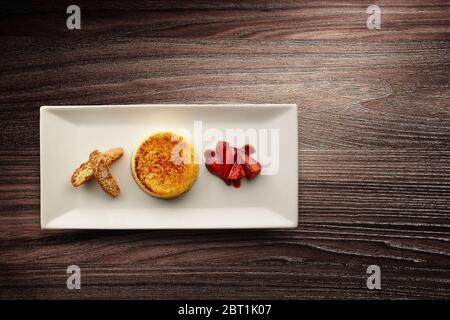 Directement au-dessus d'une nouvelle assiette de cuisine élégante avec crème brûlée aux fraises et biscotti sur fond de bois Banque D'Images