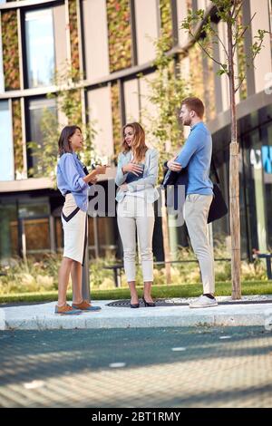 jeune femme d'affaires qui parle à deux collègues caucasiens devant un bâtiment. Banque D'Images