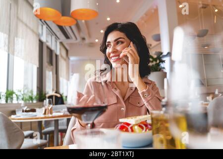 Charmante jeune femme ayant une conversation téléphonique dans un café Banque D'Images