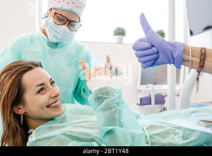 Une patiente heureuse souriant et montrant un geste de pouce avec des dentistes professionnels lors d'un rendez-vous dans un bureau moderne en clinique Banque D'Images