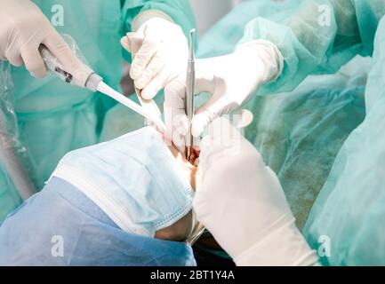 De la culture ci-dessus dentistes professionnels en latex gants utilisant des outils propres pour effectuer la procédure orale sur le patient méconnaissable dans la clinique contemporaine Banque D'Images