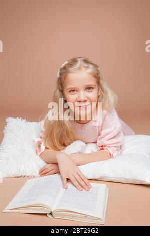 la blonde fille se trouve sur un fond rose et lit un livre Banque D'Images