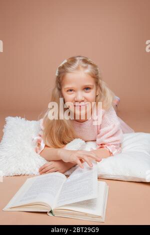 la blonde fille se trouve sur un fond rose et lit un livre Banque D'Images