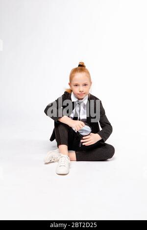 fille dans un costume noir d'affaires est assis à pattes croisées et tient une loupe Banque D'Images