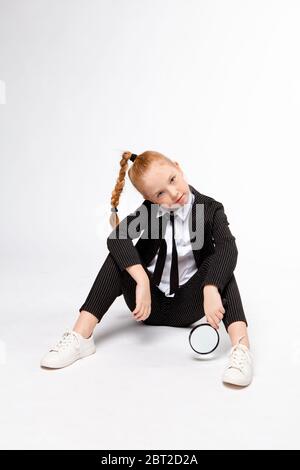 fille dans un costume noir d'affaires est assis à pattes croisées et tient une loupe Banque D'Images