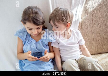 Les enfants ont un bon moment à la maison concept. Fermez le petit frère et la sœur jouant avec la tablette. Enfants assis sur un canapé, jouant avec une tablette. Les enfants jouent un Banque D'Images