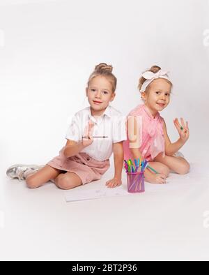 deux filles sont assises à pattes croisées et s'attirent sur du papier avec des stylos à pointe feutre. Banque D'Images