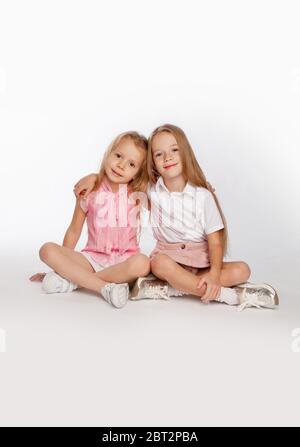 Deux jolies amies sont assises près du corps et les jambes croisées sur le sol dans le studio. Portrait lumineux. Banque D'Images