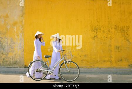 Deux belles femmes portant le traditionnel Ao dai marchant le long de la rue, Hoi an, Vietnam Banque D'Images
