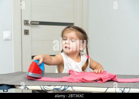 une jolie petite fille joue une femme au foyer, repassant les vêtements des enfants avec un fer à repasser. auto-isolation et quarantaine avec les jeunes enfants Banque D'Images