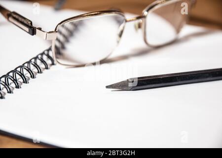 Image de fond du bureau avec bloc-notes et fournitures sur bureau en bois, lunettes fines et crayon noir. Banque D'Images