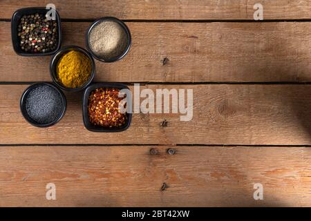 Cinq petits bols avec mélange de poivrons, poivre blanc, piments rouges secs, graines de chiots et curry sur le côté gauche d'une surface en bois Banque D'Images