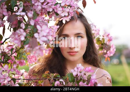 Une jeune belle fille se tient dans les fleurs roses de Un Apple Tree en gros plan Banque D'Images