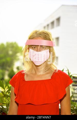 Femme avec un masque chirurgical rose et une visière protectrice sur son visage, sur fond urbain. Concept de l'épidémie de COVID-19, quarantaine pour le public Banque D'Images