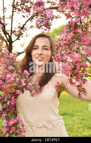 Une jeune belle fille sourit et tient une pomme en fleur branche au soleil Banque D'Images