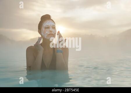 Femme debout dans le Blue Lagoon mettant de la boue sur son visage, Islande Banque D'Images