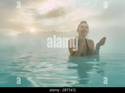 Femme debout dans le Blue Lagoon mettant de la boue sur son visage, Islande Banque D'Images