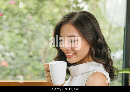 Femme indépendante tenant une tasse à café et utilisant un ordinateur portable sur une table dans un café-restaurant Banque D'Images