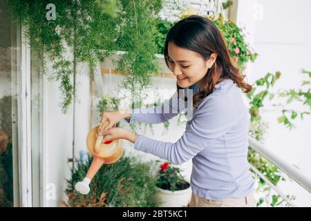 Happy Young Asian Woman femme au foyer arrosage des fleurs sur le balcon Banque D'Images