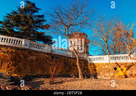 Pont en pierre historique avec branches d'arbres, pins et tour en pierre de deux étages au-dessus de lumières jaunes du coucher du soleil. Banque D'Images