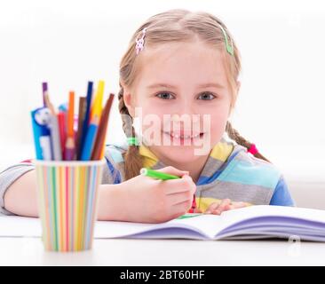 Petite jolie fille drôle jouant avec des marqueurs colorés à la table de travail, sur fond blanc Banque D'Images