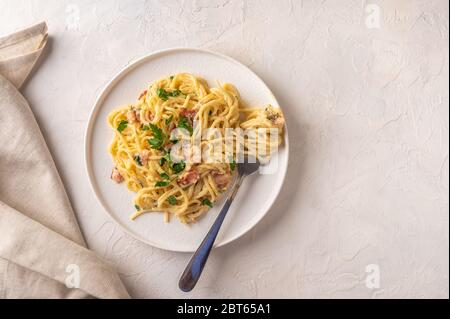 Classique maison pâtes carbonara italienne avec bacon, œufs, parmesan sur plaque céramique légère avec fourchette et serviette sur table légère. Copier l'espace Banque D'Images