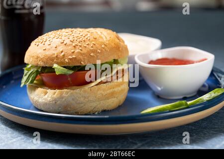 Un hamburger maison servi avec un coca et un bol de sauce tomate et des tranches de concombre Banque D'Images