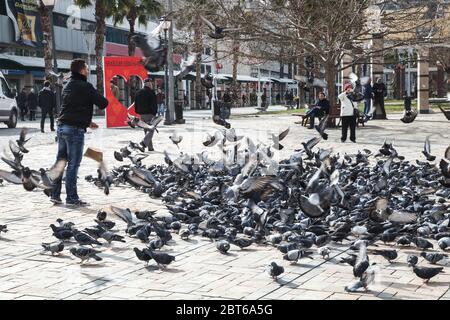 Izmir, Turquie - 12 février 2015 : un homme nourrit des pigeons sur la place Konak, dans la vieille partie centrale historique de la ville d'Izmir, les gens ordinaires marchent dans la rue Banque D'Images