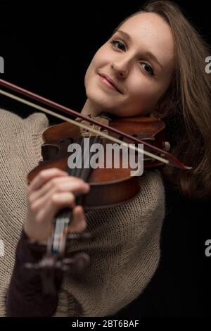 Violoniste souriante, jouant un violon baroque classique dans un portrait de près, avec un accent sur son visage sur un fond noir Banque D'Images