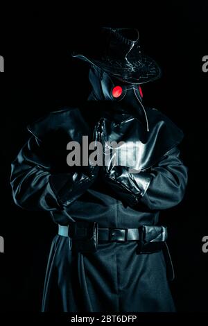 Homme en costume de médecin de peste avec masque de corbeau priant avec les mains isolées sur fond noir. Masque créepy, concept de costume historique. Épidémie Banque D'Images