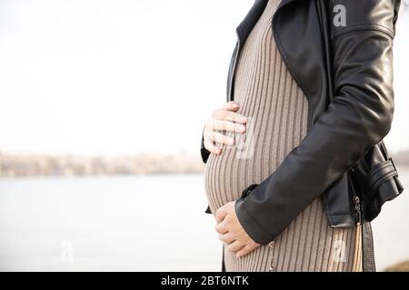 La femme enceinte en robe tient les mains sur l'estomac. Grossesse, concept de maternité. Fille enceinte dans le parc Banque D'Images