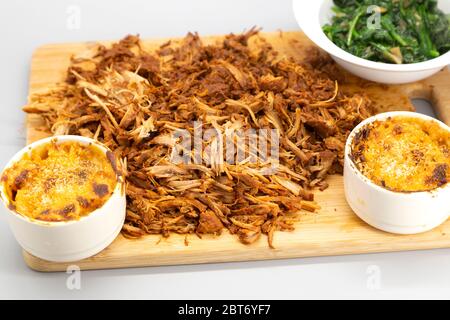 Porc tiraillé à la maison servi râpé sur un panneau de bois. Le plat est servi avec du mac et du fromage et des épinards sautés. Banque D'Images