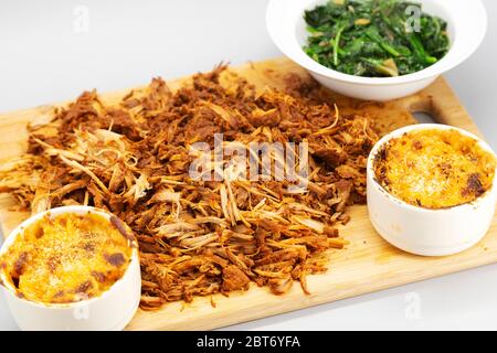 Porc tiraillé à la maison servi râpé sur un panneau de bois. Le plat est servi avec du mac et du fromage et des épinards sautés. Banque D'Images