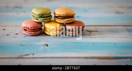 Gros plan de gâteaux de macarones faits main colorés et savoureux - biscuits au sucre sur une table en bois bleu tendance - chocolat et concept d'énergie alimentaire Banque D'Images