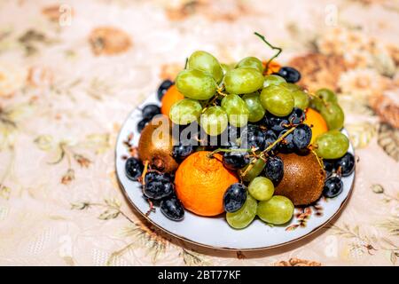 Gros plan de l'ensemble des oranges mandarines satsuma non pelées et des raisins verts rouges fruits tas sur plaque bol en hiver automne avec tabecloth ta Banque D'Images