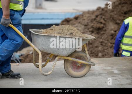 Bucarest, Roumanie - 8 mai 2020 : détails avec un ouvrier de construction poussant une brouette sur un chantier de construction. Banque D'Images