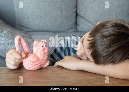 Un enfant triste joue avec un chat rose jouet fait de fil. L'enfant joue allongé sur la table. Banque D'Images