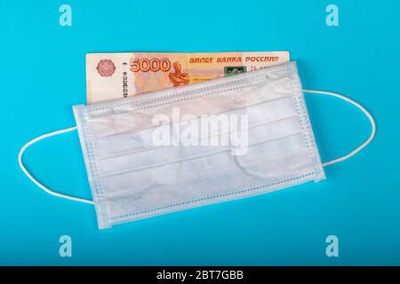 Le masque médical protecteur repose sur l'argent sur un fond cyan. Vente de masques médicaux. Le concept d'augmenter le prix des masques médicaux. Banque D'Images