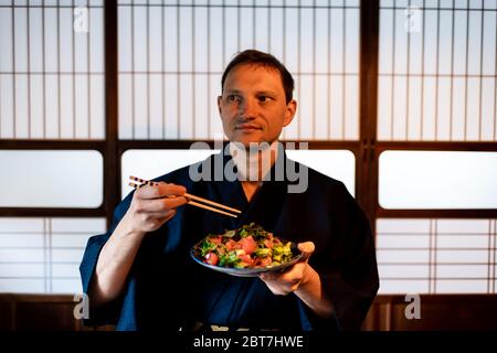 Maison japonaise traditionnelle ou restaurant ryokan avec un touriste dans un kimono ou yukata manger à partir d'une assiette de salade et de fond de portes de shoji Banque D'Images