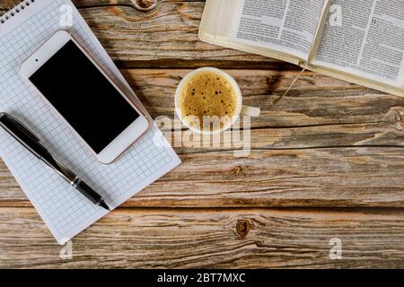 Los Angeles CA US 16 MAI 2020: Étude du matin avec la Bible sainte ouverte avec tasse de café noire sur smartphone et stylo sur bloc-notes spirale sur fond en bois Banque D'Images