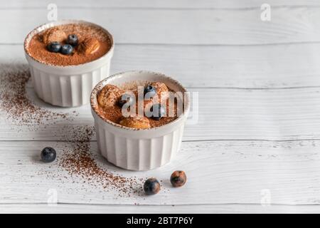 Délicieux dessert tiramisu avec biscuits au cacao et savoyardi dans des pots en céramique blanche avec copyspace sur fond gris Banque D'Images