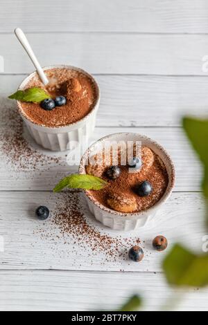 Dessert tiramisu classique avec bleuets, menthe dans un pot blanc sur fond gris. Concept de Flat Lay. Verticale Banque D'Images