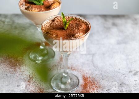 Gros plan d'un gâteau italien traditionnel tiramisu sucré avec des baies de menthe et de myrtille en verre sur du gris Banque D'Images