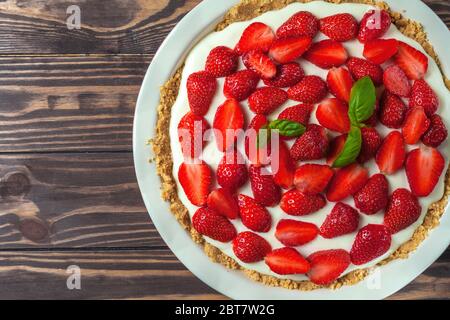 Cheesecake aux fraises avec feuilles de basilic, dans un plat de cuisson en céramique rouge sur fond de bois Banque D'Images