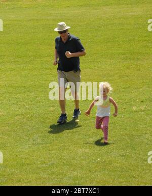 Grand-père court sur une pente herbeuse avec petite-fille à l'extérieur. Banque D'Images