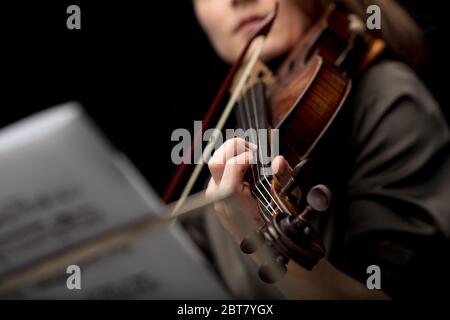 Une violoniste jouant un violon baroque classique regardée au-delà d'une partition musicale sur un stand avec une attention sélective à ses doigts sur les cordes Banque D'Images