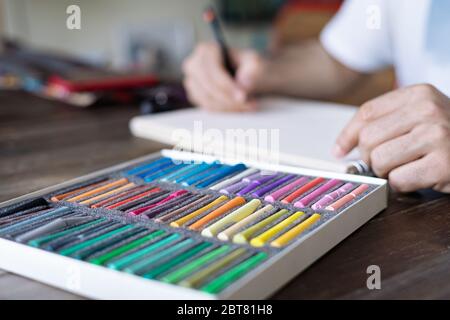 personne, artiste peignant avec une craie pastel sur une feuille de papier blanche et une pelette sur la table en bois Banque D'Images