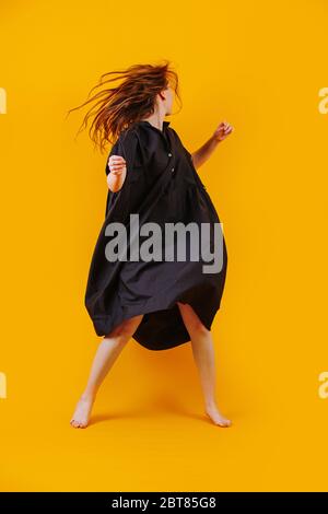 La fille danse dans une robe noire. Photo de studio sur fond jaune Banque D'Images