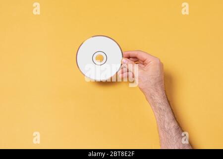 Main mâle tenant un CD-DVD devant un fond jaune, modèle de série maquette prêt pour votre conception, chemin de sélection de couverture inclus Banque D'Images